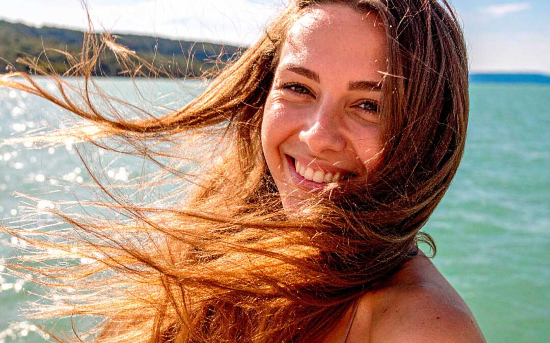Frau mit glänzenden Echthaar-Extensions am Balaton in Ungarn – perfekte Sommerhaare trotz Sonne, Wasser und Wind